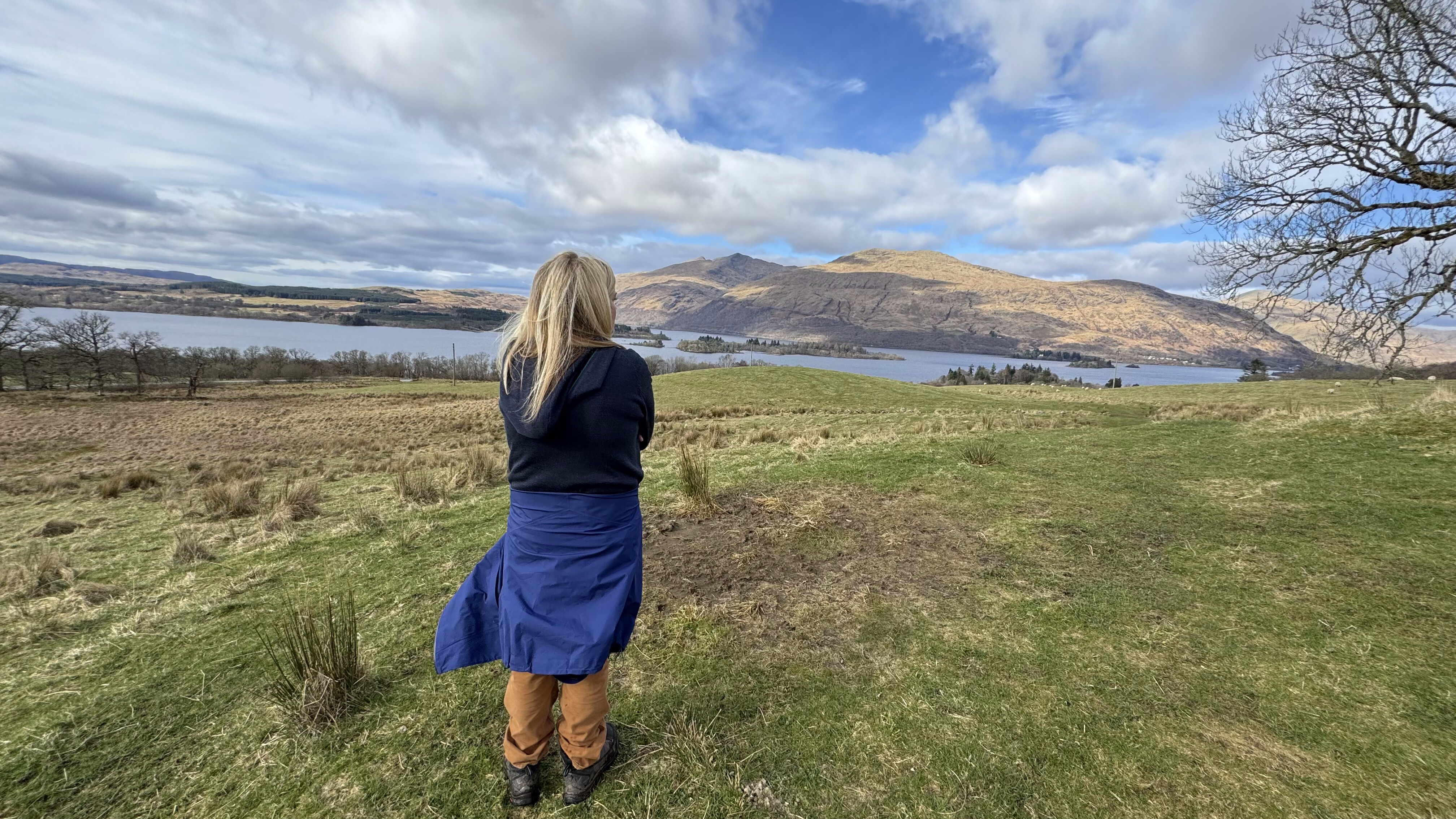 Jen standing on a hillside looking out over a Scottish loch, with hills rolling into the distance.